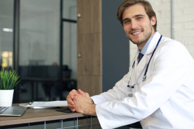 Hastane koridorunda yakışıklı genç doktor kameraya bakıyor, gülümsüyor.