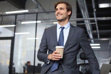 Genç yakışıklı işadamı ofis ortamında gülümsüyor.