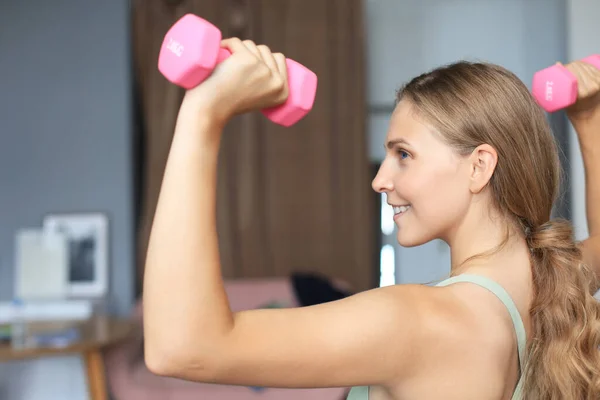 Giovane bella ragazza sportiva in leggings e un top fa esercizi con manubri. Uno stile di vita sano. Una donna va a fare sport a casa. — Foto Stock