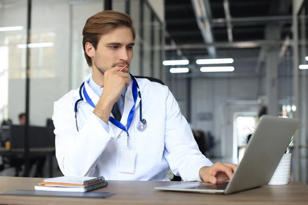 医師は タブレット上の患者の個人的なファイルを読み取り ノートパソコンにデータを書き込み聴診器と白い医療均一 — ストック写真