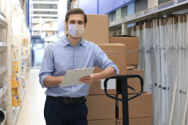 Portrait of handsome warehouse wears medical mask during epidemy. Worker in a cash and carry wholesale store clipart