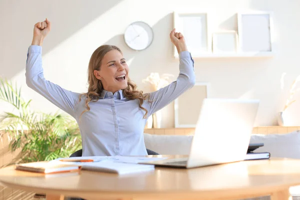 幸せな起業家の女性は良いニュースを読んで机に座って 手を上げて喜びを表現 — ストック写真