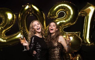 Şampanya içen iki genç bayan. Siyah arka planda izole edilmiş balonlu kızlar 2021 yılbaşı partisinde eğleniyorlar.