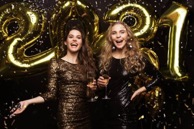 Şampanya içen iki genç bayan. Siyah arka planda izole edilmiş balonlu kızlar 2021 yılbaşı partisinde eğleniyorlar.