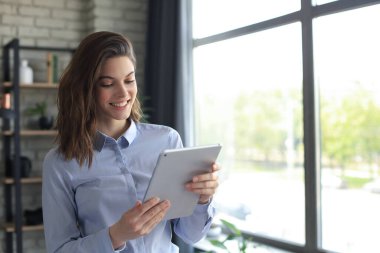 Ev ofisinde tablet üzerinde çalışan çekici, gülümseyen bir kadın.