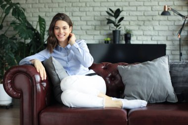 Kanepede rahatça oturup gülümseyen bir kadın. Güzel beyaz bir kız dinleniyor.