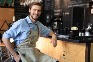 Kafe sahibi. Mutlu adam tezgahın yanında oturuyor, gülümsüyor.
