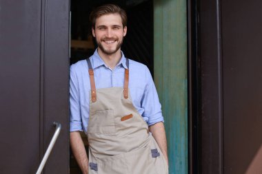 Yakışıklı ve kendine güvenen kafe sahibi kapıda duruyor. Kollarını kavuşturup kameraya gülümseyen genç bir adam.