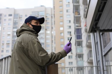 Evin girişinde paketli yüz maskesi olan kurye, bilgiyi akıllı telefondan doğruladı