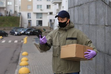 Evin girişinde paketli yüz maskesi olan kurye, belgelerdeki bilgiyi doğruluyor.