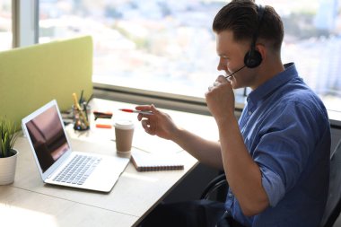 Laptop, hizmet ve müşteri danışma konsepti kullanırken, iş yerinde, kulaklık takmış neşeli genç telefon operatörü.