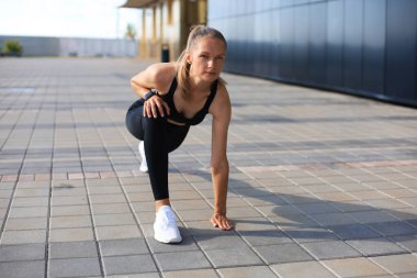 Spor elbiseli atletik bir kadın açık havada koşarken başlangıç çizgisinde duruyor.