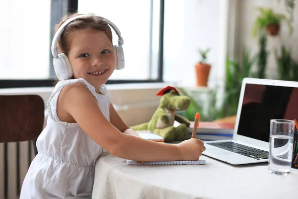 Distance learning. Cheerful little girl girl in headphones using laptop studying through online e-learning system