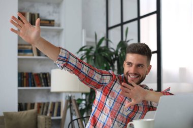 Yakışıklı iş adamı ev ofisinde kollarını havada tutuyor ve neşeli bir ifade sergiliyor.