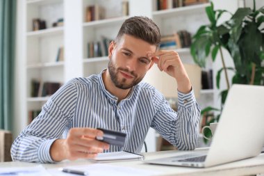 Gülümseyen adam ofiste oturuyor ve kredi kartıyla ödüyor.