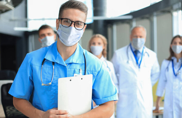 Male doctor in medical mask with group of happy successful colleagues also in preventive masks.