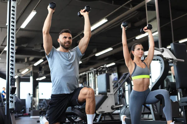 Çekici sporcular spor salonunda dambıllarla çalışıyor.
