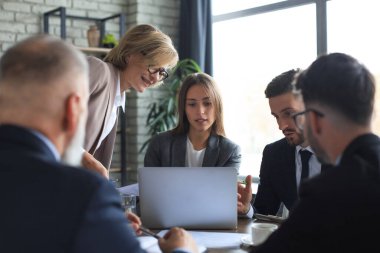 Girişim ekibi, modern parlak ofis içinde toplantı ve dizüstü bilgisayar üzerine çalışıyor