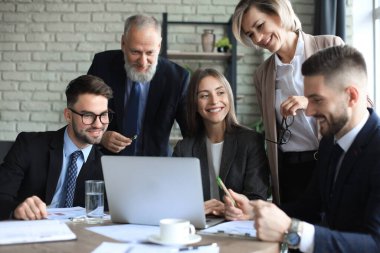 Girişim ekibi, modern parlak ofis içinde toplantı ve dizüstü bilgisayar üzerine çalışıyor