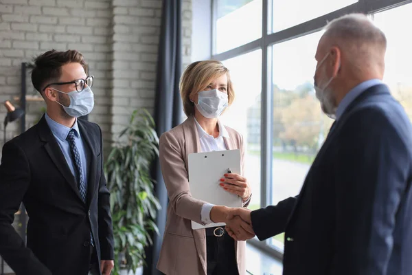 Business people in medical masks shaking hands, finishing up a meeting