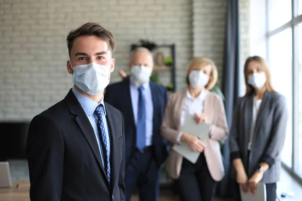 의료용 마스크를 사무실 뒤에서 동료들 일하는 사업가 — 스톡 사진