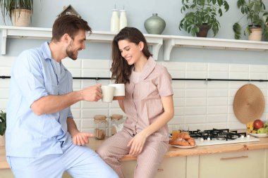 Pijamalı güzel bir çift evde yemek pişirirken birbirlerine bakıp gülümsüyor.
