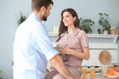 Pijamalı güzel bir çift evde yemek pişirirken birbirlerine bakıp gülümsüyor.