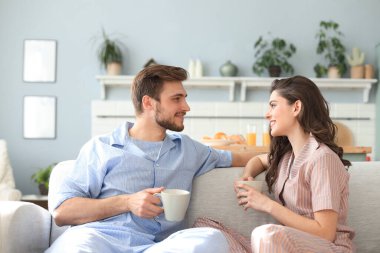 Pijamalı güzel bir çift birbirine bakıyor ve oturma odasındaki kanepede gülümsüyor.