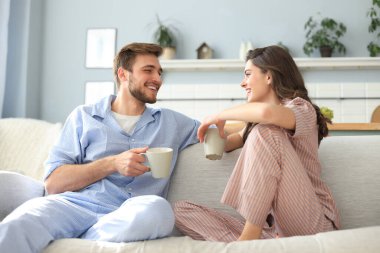 Pijamalı güzel bir çift birbirine bakıyor ve oturma odasındaki kanepede gülümsüyor.