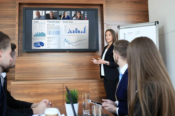 Business team at office, businessman presenting and discussing successful financial report of their company, on screen of plasma TV at meeting room, talking to his colleagues in video conference.