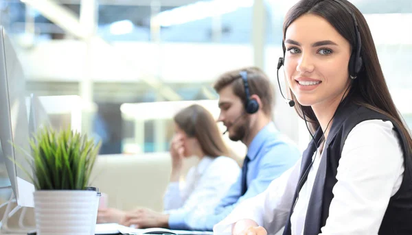 Leende kvinnlig callcenter operatör gör sitt jobb med ett headset medan du tittar på kameran. — Stockfoto