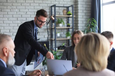 Girişim ekibi, modern parlak ofis içinde toplantı ve dizüstü bilgisayar üzerine çalışıyor