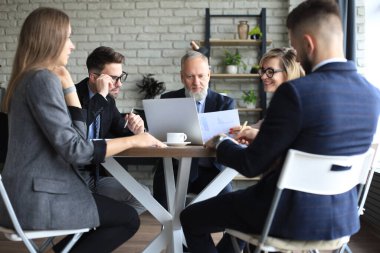 İş adamlarından oluşan bir ekip yaratıcı ofiste masada tartışıyor.