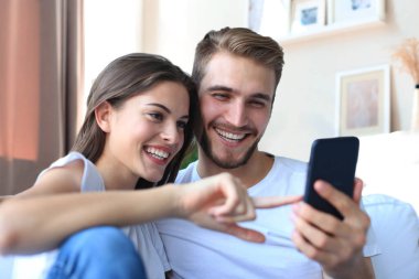 Mutlu çift, evdeki koltukta oturmuş akıllı bir telefonla medyadan zevk alıyor.