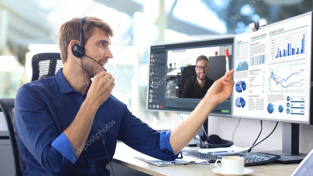 Businessman in headphones talking to his colleagues in video conference. Multiethnic business team working from office using computer PC, discussing financial report of their company.
