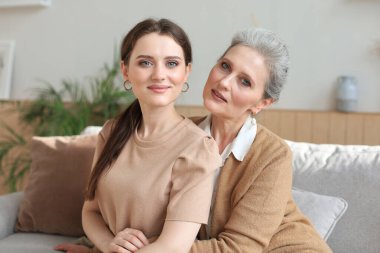 Evde sarılan yaşlı anne ve yetişkin kızın portresi. Mutlu kıdemli anne ve yetişkin kız kanepede sevgiyle kucaklaşıyorlar.