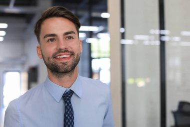 Genç yakışıklı işadamı ofis ortamında gülümsüyor.