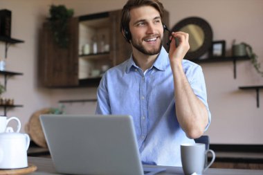 Gülümseyen işadamı, video konferansında meslektaşlarını selamlıyor ve evden uzakta pazarlık yapıyor.