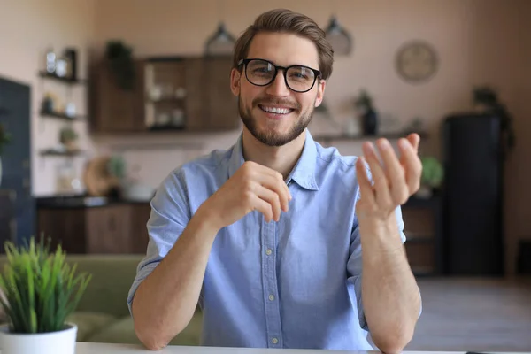 Confident happy businessman in eyeglasses sitting at home workplace and looking at camera