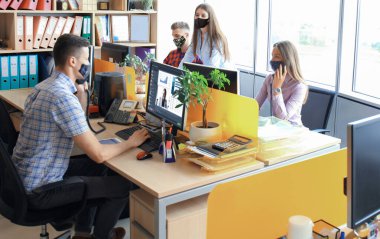 Koruyucu maskeler takarak iş kurma ekibi modern parlak ofis içi beyin fırtınasında buluşup bilgisayarlar üzerinde çalışıyor.