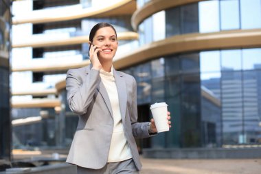 Takım elbiseli güzel bir kadın akıllı telefon kullanıyor ve dışarıda dururken gülümsüyor.