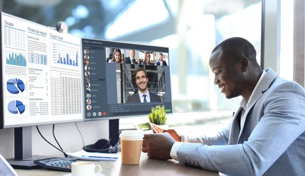 Afrikanischer Geschäftsmann im Gespräch mit seinen Kollegen in Videokonferenz. Multiethnisches Business-Team, das vom Büro aus mit dem PC arbeitet und den Finanzbericht seines Unternehmens diskutiert. — Stockfoto