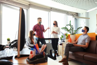 Koruyucu maskeler takarak iş kurma ekibi modern parlak ofis içinde buluşup yeni projeyi tartışıyor..