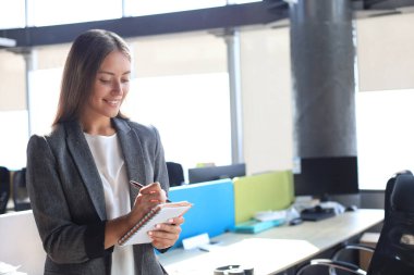 Yoğunlaşmış genç bir kadın ofiste çalışırken bir şeyler yazıyor.