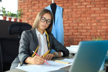 Güzel genç tasarımcı stüdyosunda otururken notlar alıyor.