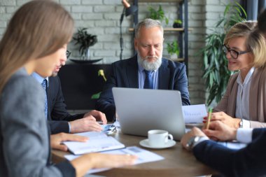 Girişim ekibi, modern parlak ofis içinde toplantı ve dizüstü bilgisayar üzerine çalışıyor