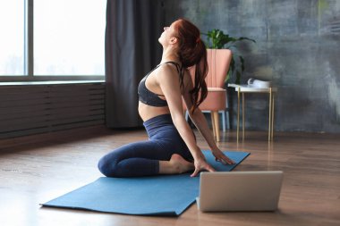 Sportif, ince kadın dizüstü bilgisayarın önünde yoga yapıyor, online dersler izliyor. Sağlıklı yaşam tarzı