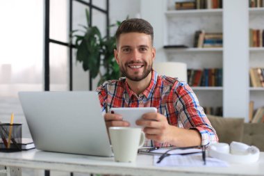 Çekici genç adam evdeki masada oturuyor ve sosyal ağları kontrol etmek için cep telefonunu kullanıyor.