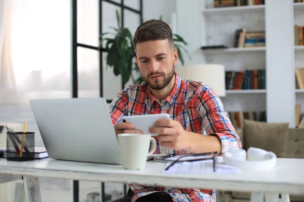 Attraktiv Ung Man Sitter Vid Skrivbordet Hemmakontoret Och Använder Mobiltelefon — Stockfoto