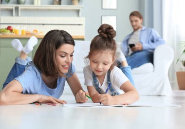 Mutlu anne gülümseyen kız sıcak zeminde uzanıyor yaratıcı aktivitelerin tadını çıkarıyor, albümle kalemler çiziyor..